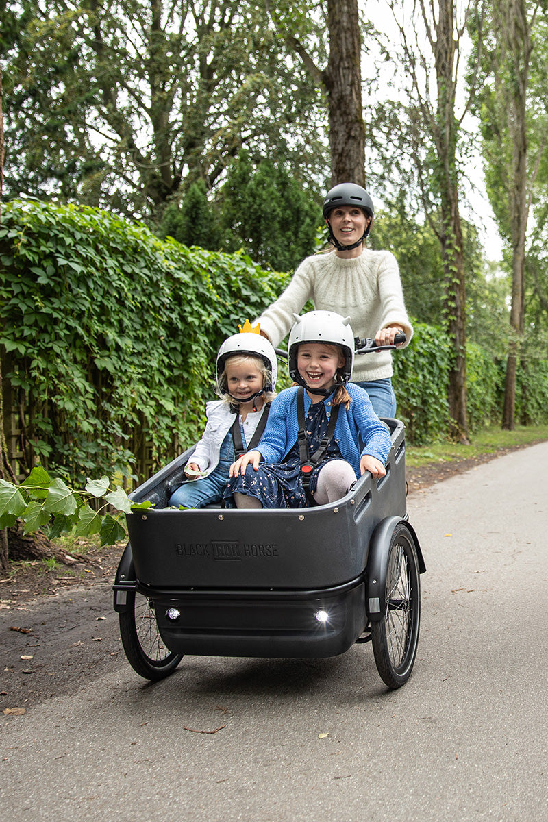 Parent riding a Black Iron Horse cargo trike with two laughing children in the front box