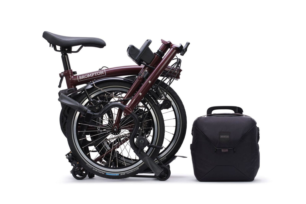 Brompton Electric C Line in plum red — fully folded beside the battery bag
