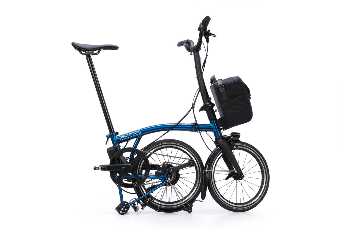 Brompton Electric P Line in pacific blue lacquer — mid-fold with the rear wheel tucked under