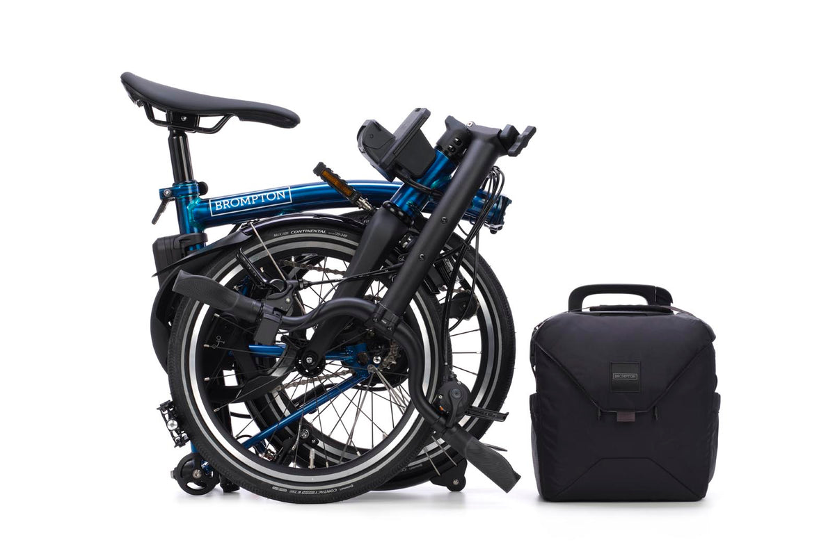 Brompton Electric P Line in pacific blue lacquer — fully folded beside the battery bag