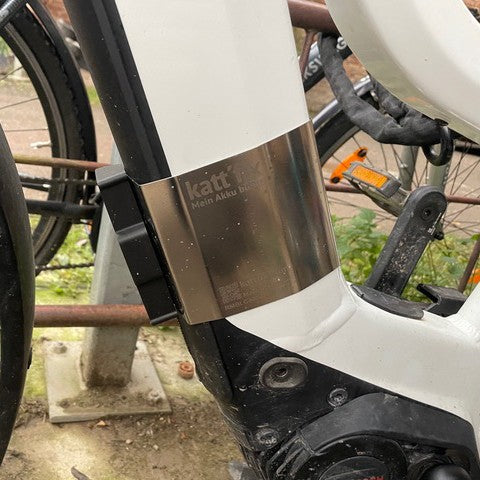 Kattfix battery lock secured around the downtube battery of a white Riese & Muller e-bike parked outdoors