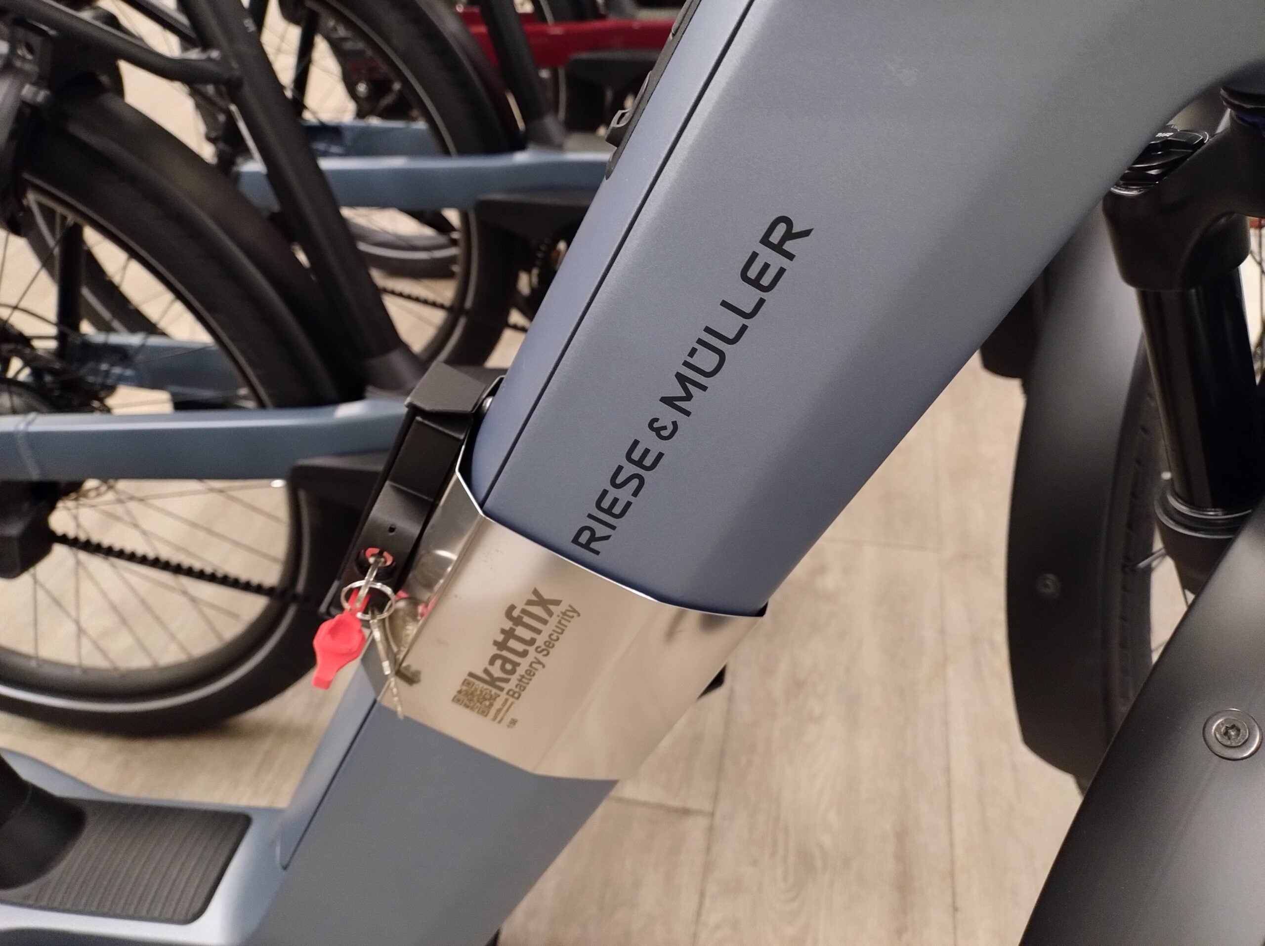 Kattfix stainless battery band with red key on the downtube battery of a blue-grey Riese & Muller Nevo