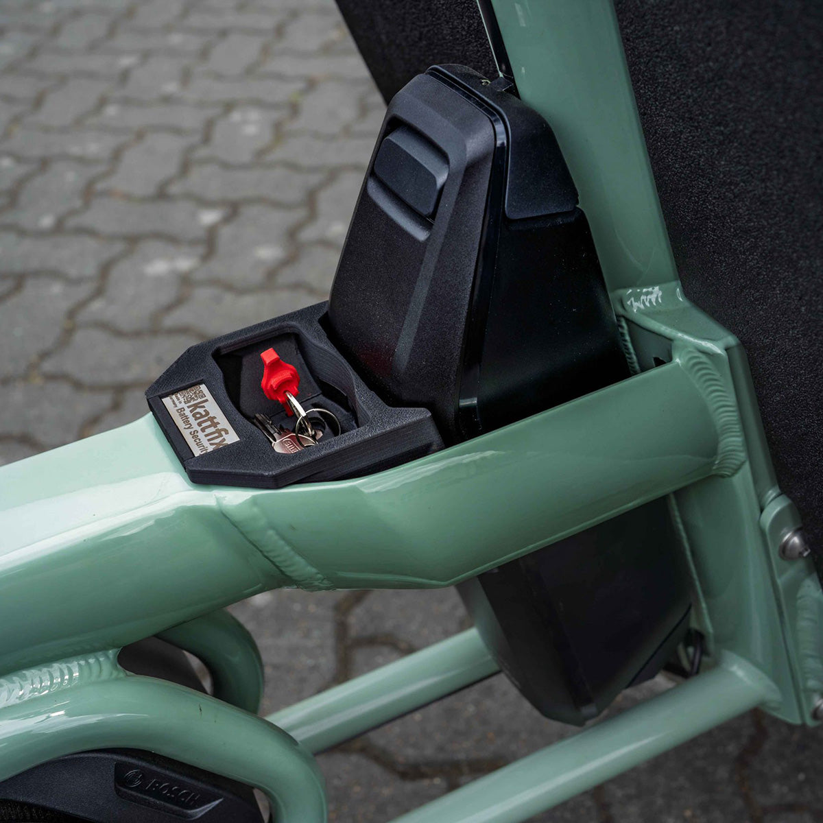 Kattfix battery lock open with the red key in its cylinder, fitted on a sage-green Urban Arrow